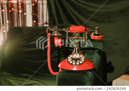 Vintage red telephone with round dial, positioned on dark green velvet. nostalgic touch with its intricate brass details and curly cord. Close-up of retro red telephone, brass dialer, receiver vividly Vintage red telephone with round dial, positioned on dark green velvet. nostalgic touch with its intricate brass details and curly cord. Close-up of retro red telephone, brass dialer, receiver vividly 142626240