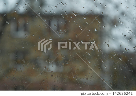 Window covered with rain droplets, water drops clinging to glass, blurry house in background, rainy day scene, abstract texture, detail, closeup, natural weather, humidity, urban environment Window covered with rain droplets, water drops clinging to glass, blurry house in background, rainy day scene, abstract texture, detail, closeup, natural weather, humidity, urban environment 142626241