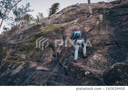 Rock climber climbing high rock wall, extreme sport outside, alpinism equipment 142626408