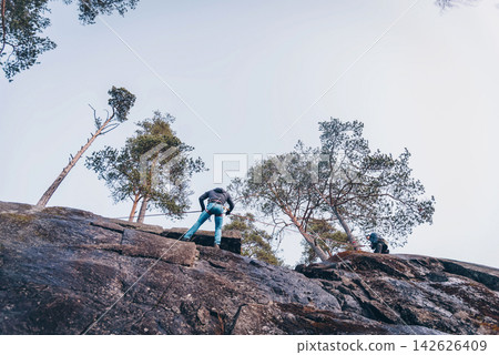 Rock climber climbing high rock wall, extreme sport outside, alpinism equipment 142626409