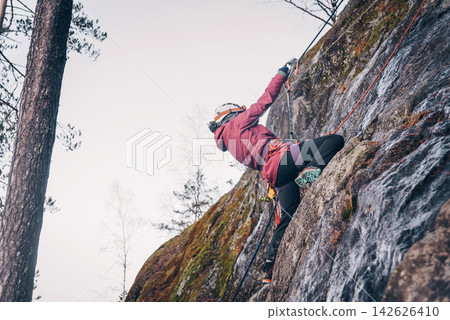 Rock climber climbing high rock wall, extreme sport outside, alpinism equipment 142626410