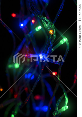 Colorful LED fairy lights tangled against a dark black background, glowing in vibrant shades of green, blue, yellow, and red. Abstract holiday illumination and decoration background Colorful LED fairy lights tangled against a dark black background, glowing in vibrant shades of green, blue, yellow, and red. Abstract holiday illumination and decoration background 142627000