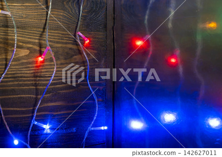 Colorful LED Christmas fairy lights glowing on a dark brown wooden plank background, creating a festive holiday atmosphere. Abstract holiday illumination and decoration background Colorful LED Christmas fairy lights glowing on a dark brown wooden plank background, creating a festive holiday atmosphere. Abstract holiday illumination and decoration background 142627011