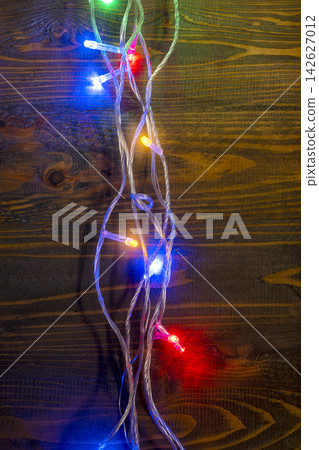Colorful LED Christmas fairy lights glowing on a dark brown wooden plank background, creating a festive holiday atmosphere. Abstract holiday illumination and decoration background Colorful LED Christmas fairy lights glowing on a dark brown wooden plank background, creating a festive holiday atmosphere. Abstract holiday illumination and decoration background 142627012