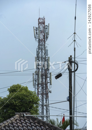 Telecommunication tower with cellular antennas standing tall behind utility poles and green trees under a clear sky. Concept of communication network and connection technology Telecommunication tower with cellular antennas standing tall behind utility poles and green trees under a clear sky. Concept of communication network and connection technology 142627086