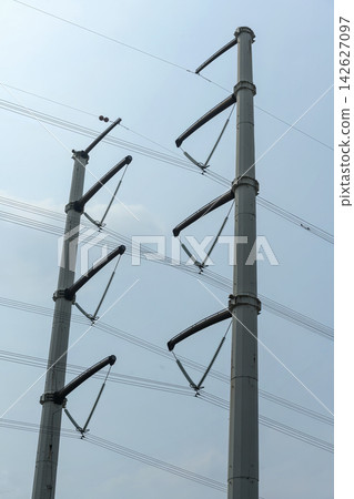 Two modern steel power transmission poles with high-voltage lines and insulators against a clear sky. Concept of the electricity energy industry Two modern steel power transmission poles with high-voltage lines and insulators against a clear sky. Concept of the electricity energy industry 142627097