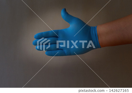 A person's hand in a blue medical glove extends their hand in greeting.  142627165