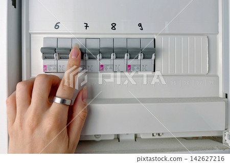 Close-up of a hand checking circuit breakers in a residential electrical distribution panel with multiple labeled switches and protective devices. Close-up of a hand checking circuit breakers in a residential electrical distribution panel with multiple labeled switches and protective devices. 142627216