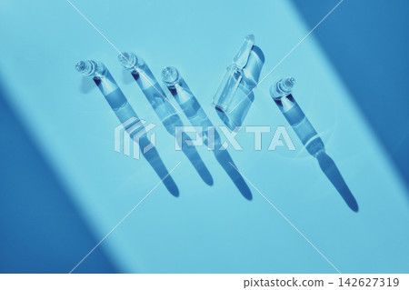 Glass ampoules containing liquid medicine for injection or vaccination on a blue background 142627319