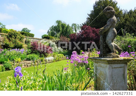 英國一座美麗的英式花園，四周環繞著石雕和花朵。 142627331