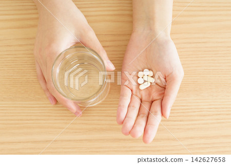 一隻手拿著杯子,手掌裡裝著藥丸,手掌攤在桌上。 一隻手拿著杯子,手掌裡裝著藥丸,手掌攤在桌上。 142627658