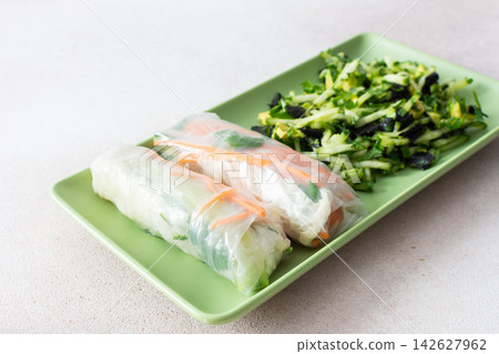 Rolls with red fish, carrots, and cucumbers in rice paper sit next to a fresh salad with cucumbers and avocado. This meal is great for breakfast or lunch and is gluten-free 142627962