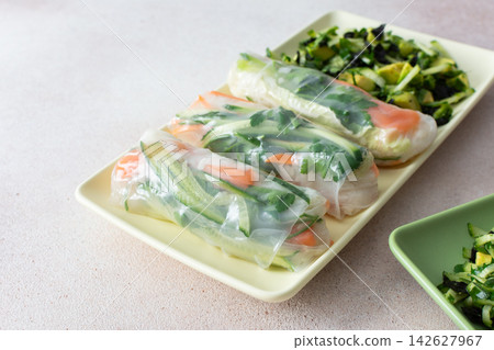 Rolls with red fish, carrots, and cucumbers in rice paper sit next to a fresh salad with cucumbers and avocado. This meal is great for breakfast or lunch and is gluten-free Rolls with red fish, carrots, and cucumbers in rice paper sit next to a fresh salad with cucumbers and avocado. This meal is great for breakfast or lunch and is gluten-free 142627967