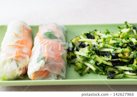 Rolls with red fish, carrots, and cucumbers in rice paper sit next to a fresh salad with cucumbers and avocado. This meal is great for breakfast or lunch and is gluten-free Rolls with red fish, carrots, and cucumbers in rice paper sit next to a fresh salad with cucumbers and avocado. This meal is great for breakfast or lunch and is gluten-free 142627968