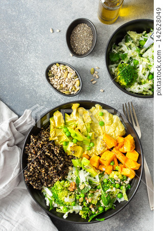 A quinoa bowl is arranged with roasted pumpkin, hummus, and a fresh salad. Plates are set on a table with utensils. Sunshine comes through the window A quinoa bowl is arranged with roasted pumpkin, hummus, and a fresh salad. Plates are set on a table with utensils. Sunshine comes through the window 142628049