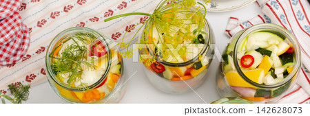 Jars filled with zucchini and other vegetables are arranged on the kitchen counter for canning. Fresh ingredients are used for winter preservation in a cozy kitchen, banner Jars filled with zucchini and other vegetables are arranged on the kitchen counter for canning. Fresh ingredients are used for winter preservation in a cozy kitchen, banner 142628073