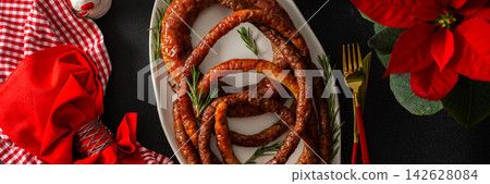 A Christmas table is set with fried pork sausage in the center. Red flowers and festive decorations surround the food as families gather to celebrate during the evening, banner A Christmas table is set with fried pork sausage in the center. Red flowers and festive decorations surround the food as families gather to celebrate during the evening, banner 142628084