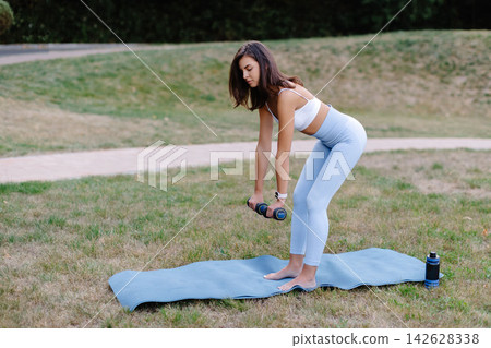 Young woman exercising with dumbbells in a park, promoting healthy lifestyle and fitness Young woman exercising with dumbbells in a park, promoting healthy lifestyle and fitness 142628338