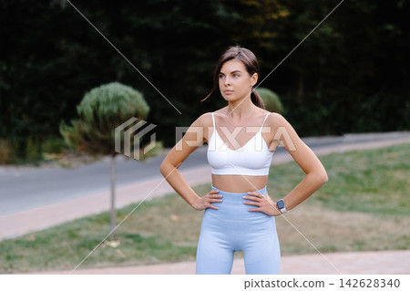Confident sportswoman posing with hands on hips in a park Confident sportswoman posing with hands on hips in a park 142628340