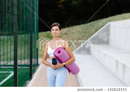 Young woman holding yoga mat and water bottle going to fitness training Young woman holding yoga mat and water bottle going to fitness training 142628355