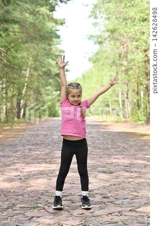 Young girl raises arms on cobblestone forest road, 142628498