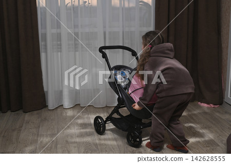 Cute female kid interacts with pink pram at home. Cute female kid interacts with pink pram at home. 142628555