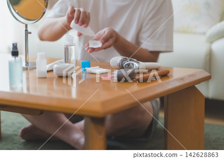 一位四十多歲的男子坐在擺放著化妝品的桌子前,將乳液塗抹在化妝棉上。 (男士美容) 一位四十多歲的男子坐在擺放著化妝品的桌子前,將乳液塗抹在化妝棉上。 (男士美容) 142628863