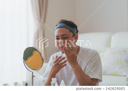 一位40歲的男子麵帶微笑,雙手各用棉片敷在臉頰上。男人的美 一位40歲的男子麵帶微笑,雙手各用棉片敷在臉頰上。男人的美 142629085