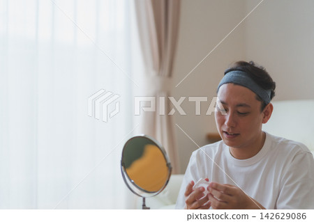一位40歲的男子在桌面鏡子前準備好護膚,手裡拿著化妝棉。 一位40歲的男子在桌面鏡子前準備好護膚,手裡拿著化妝棉。 142629086