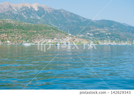 Scenic view of the Gulf of Nidri in Lefkada, showcasing calm waters, sailboats anchored along the shore, and lush green hills under a clear blue sky Scenic view of the Gulf of Nidri in Lefkada, showcasing calm waters, sailboats anchored along the shore, and lush green hills under a clear blue sky 142629343