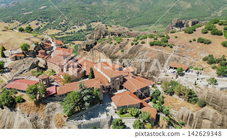 Aerial view of Meteora monasteries perched on rocky cliffs surrounded by lush green hills and valleys in Greece, showcasing traditional architecture and natural beauty of the region Aerial view of Meteora monasteries perched on rocky cliffs surrounded by lush green hills and valleys in Greece, showcasing traditional architecture and natural beauty of the region 142629348