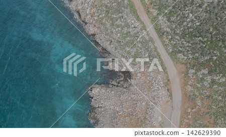 Aerial view of rocky coastline along the turquoise sea in Crete, showcasing the natural landscape with a winding road and clear blue waters reflecting sunlight Aerial view of rocky coastline along the turquoise sea in Crete, showcasing the natural landscape with a winding road and clear blue waters reflecting sunlight 142629390