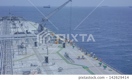View from the deck of a large cargo ship showing pipelines and machinery leading towards the horizon over the ocean with waves and cloudy sky in the background View from the deck of a large cargo ship showing pipelines and machinery leading towards the horizon over the ocean with waves and cloudy sky in the background 142629414