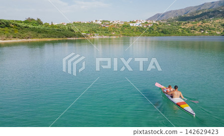 Father and daughter paddling together in a kayak on a calm lake surrounded by lush greenery and distant hills under a clear blue sky Father and daughter paddling together in a kayak on a calm lake surrounded by lush greenery and distant hills under a clear blue sky 142629423