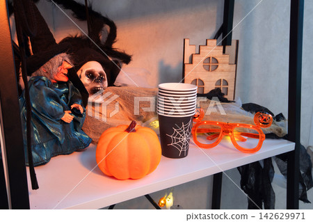 Halloween setup on a shelf with decorations including a witch doll and a pumpkin at night Halloween setup on a shelf with decorations including a witch doll and a pumpkin at night 142629971