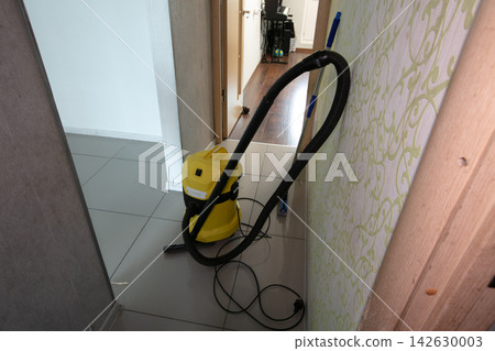 Vacuum cleaner stands in hallway during cleaning process in a home at daytime with sunlight coming through the door Vacuum cleaner stands in hallway during cleaning process in a home at daytime with sunlight coming through the door 142630003