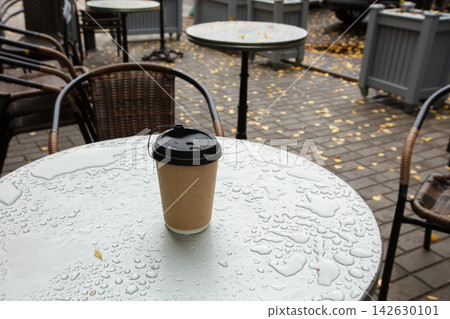 Coffee cup on a wet table in an outdoor seating area during a rainy day in a city Coffee cup on a wet table in an outdoor seating area during a rainy day in a city 142630101