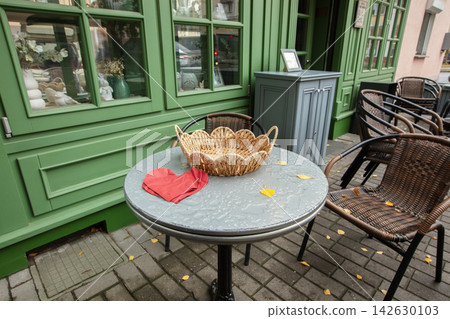 Outdoor table with woven basket and folded cloth at cafe in city during autumn morning Outdoor table with woven basket and folded cloth at cafe in city during autumn morning 142630103