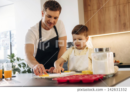 Caucasian father and son baking together in modern kitchen, rolling dough and using cookie cutters on countertop with ingredients and utensils visible Caucasian father and son baking together in modern kitchen, rolling dough and using cookie cutters on countertop with ingredients and utensils visible 142631332