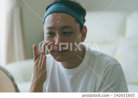 一位四十多歲的男士享受著他的美容時光,盡情享受護膚的樂趣,往臉頰上塗抹乳液。 一位四十多歲的男士享受著他的美容時光,盡情享受護膚的樂趣,往臉頰上塗抹乳液。 142631605