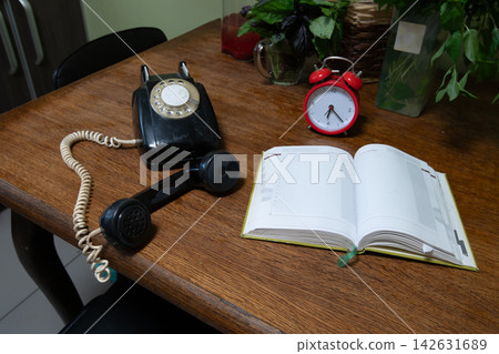 Old telephone and clock placed on a wooden table with a notebook in a simple room during the day Old telephone and clock placed on a wooden table with a notebook in a simple room during the day 142631689