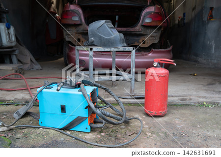 Car repair tools and fire extinguisher placed in workshop with unfinished vehicle in background 142631691
