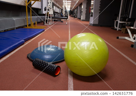 Fitness equipment is arranged on the gym floor near workout stations during a training session in the evening Fitness equipment is arranged on the gym floor near workout stations during a training session in the evening 142631776