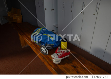 Blue backpack sits on a wooden bench next to shoes and a coffee cup in a locker room setting during the afternoon Blue backpack sits on a wooden bench next to shoes and a coffee cup in a locker room setting during the afternoon 142631782