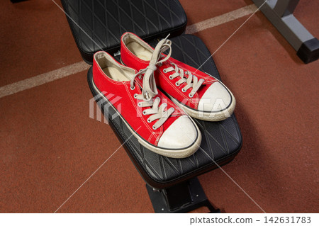 Red sneakers placed on a workout bench in a gym during a training session in the evening Red sneakers placed on a workout bench in a gym during a training session in the evening 142631783