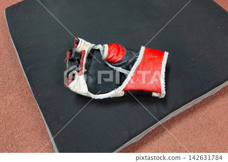 Used boxing glove resting on a black training mat in a gym after a workout session Used boxing glove resting on a black training mat in a gym after a workout session 142631784