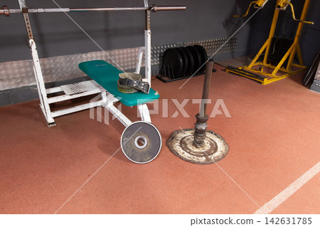Weightlifting equipment in a gym setting with a bench, weights, and a belt on a workout mat during the day Weightlifting equipment in a gym setting with a bench, weights, and a belt on a workout mat during the day 142631785