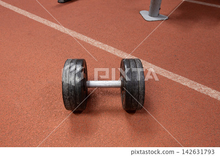 Dumbbell resting on gym floor during workout session in fitness center on a training day Dumbbell resting on gym floor during workout session in fitness center on a training day 142631793