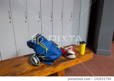 Sports gear and personal items arranged on a bench near lockers in a gym during daylight hours Sports gear and personal items arranged on a bench near lockers in a gym during daylight hours 142631794