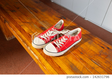 Red sneakers on a wooden bench in a simple room during daytime with soft light Red sneakers on a wooden bench in a simple room during daytime with soft light 142631796